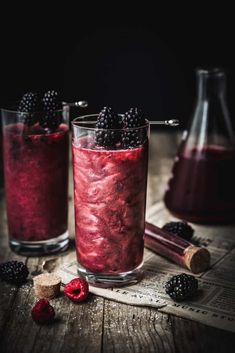 two glasses filled with raspberry and blackberries on top of a wooden table