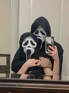 two people wearing masks are taking a selfie in front of a mirror with their cell phone