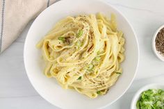 a white bowl filled with pasta next to two bowls of seasoning