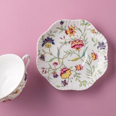 two plates with floral designs on them next to a cup and saucer in front of a pink background