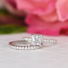 a close up of a diamond ring on a table with pink flowers in the background