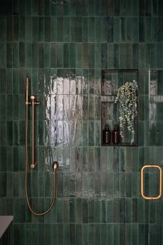 a green tiled bathroom with gold fixtures and mirrors on the wall, along with a shower head