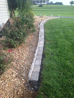 a stone path in the middle of a yard with grass and flowers on either side