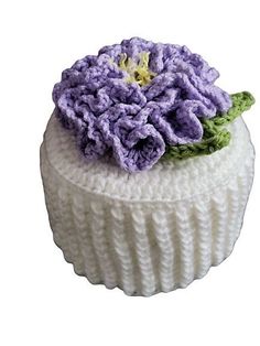 a white knitted cupcake with purple flowers on top