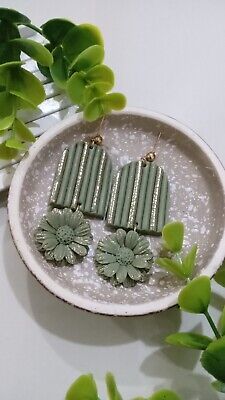 two green earrings sitting on top of a white plate next to some flowers and leaves