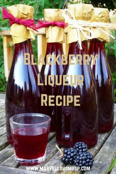 three bottles of blackberry liquor sitting on top of a wooden table next to a glass filled with blackberries