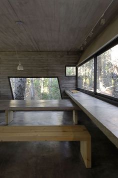 an empty room with benches and windows in the center, looking out onto trees outside