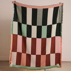 a multicolored blanket is hanging on a wooden stand in front of a wall