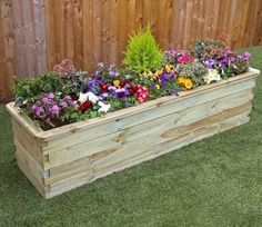 a wooden planter filled with lots of flowers on top of green grass next to a fence