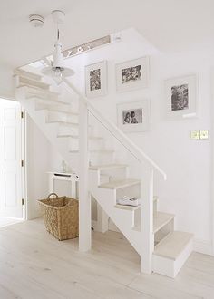 there is a white staircase with pictures on the wall and a basket in front of it