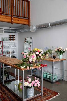 flowers are arranged in buckets on a table with an area rug and stairs to the second floor