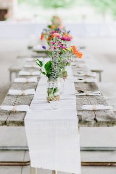 a long table with flowers in vases sitting on it's side, along with napkins and place mats