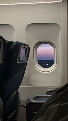 an airplane seat with the window open looking out at the ocean and sunset in the distance