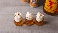 three small jars with whipped cream on them next to two bottles of booze and a bottle of beer