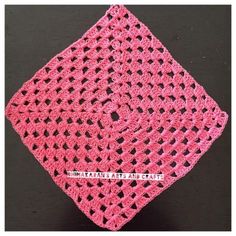 a pink crocheted square on top of a black table