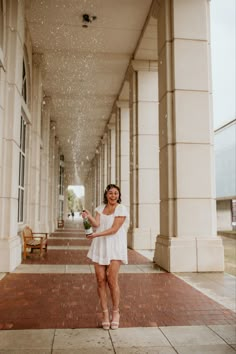 a woman in white dress standing under rain sprinkled from her hand and smiling