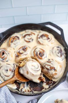 a skillet filled with cinnamon rolls on top of a white counter next to plates