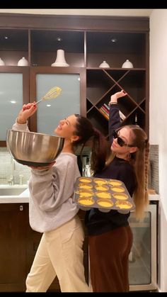 two young women are baking cookies together in the kitchen, one is holding a pan and the other holds a spatula