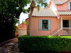 a pink house with white shutters and palm trees