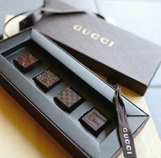 four pieces of chocolate in a black box with a brown ribbon around the top and bottom