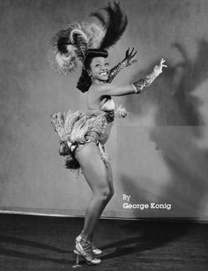 an old photo of a woman dancing with feathers on her head and legs in the air