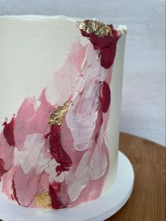 a white and pink cake with gold leaf decorations on it's side, sitting on a wooden table