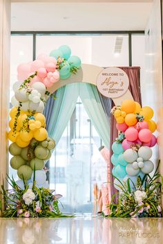 an entrance decorated with balloons and greenery for a baby shower or birthday party in pastel colors