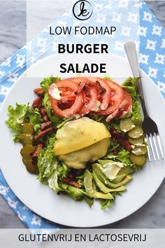 a white plate topped with salad next to a fork and knife on top of a table