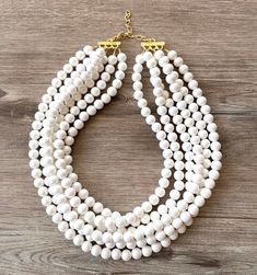 A chunky beaded multi strand statement necklace made with off white pearlized lucite beads. A very lightweight statement necklace perfect for dressing up or down. The off white color will go with everything! - 6 strands (more strands are listed)- shortest strand measures 18.5 - 20.5" long (length varies depending on the clasp)- clasp is gold stainless steel (stainless steel, sterling silver and gold filled are also available) - gold connector is lead free pewter. - 2" gold stainless steel extender chain For reference, the mannequin's neck size is 14.5". Larger quantities may be available. We use the highest quality findings to ensure a piece that will last for years to come. DLD jewelry comes with a lifetime guaranteeDana LeBlanc Designs- Handmade Jewelry Pearl White Multi-strand Beaded Necklace, White Multi-strand Necklace With Large Beads, Elegant White Jewelry With Wooden Beads, White Multi-strand Large Beads Jewelry, White Multi-strand Pearl Chain Necklace, White Multi-strand Beaded Necklace, White Multi-strand Beaded Necklaces, White Multi-strand Beaded Pearl Necklace, White Multi-strand Pearl Beaded Necklaces