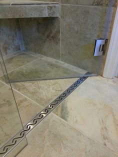 a glass shower door in a bathroom next to a tile floor and wall with a metal handle