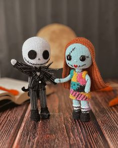 two crocheted dolls standing next to each other on a wooden table with an open book in the background