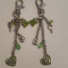 two key chains with charms attached to them on a white surface, one has a green heart and the other is a silver chain