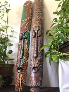 two wooden carved african masks sitting on top of a table next to a potted plant