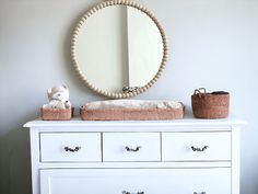 a white dresser topped with a baby crib next to a round mirror