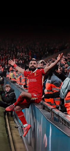 a man sitting on top of a wall in front of an audience at a soccer game