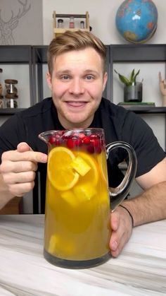 a man holding up a pitcher of liquid with fruit in it and smiling at the camera