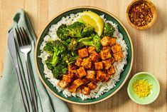 a plate with rice, broccoli and tofu on it next to a fork