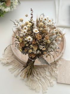 a bouquet of dried flowers sitting on top of a white table next to a wooden plate