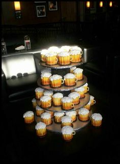 there are many cupcakes on the table with beer mugs in them and one is stacked high