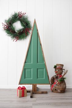 a small christmas tree sitting next to a green door with a wreath on the top