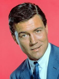 a man in a blue suit and tie posing for a photo against a red background