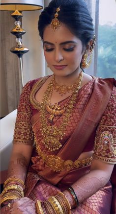 a woman in a red and gold sari sitting down with her hands on her knees