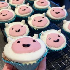 cupcakes with pink frosting and white icing decorated like animals are on a cooling rack