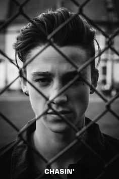 black and white photo of a young man behind a chain link fence