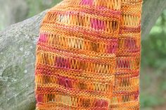 an orange and pink crocheted shawl hanging from a tree