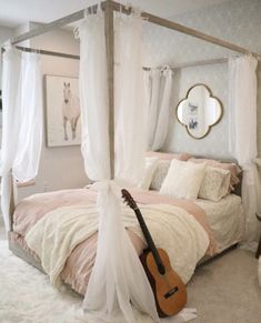 a bedroom with a four poster bed, white curtains and a guitar on the floor