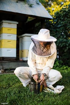 a man kneeling down in the grass with a bucket and beehive behind him