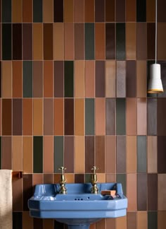 a blue sink sitting next to a wall covered in brown and tan tiles on top of a wooden floor