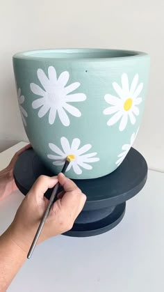 a person is painting a flower pot with a paintbrush on top of the bowl