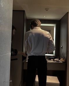 a man in a white shirt and black pants is standing in front of a mirror